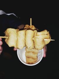 Close-up of hand holding ice cream cone against black background