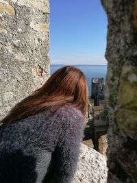 Rear view of woman standing on rock against clear sky