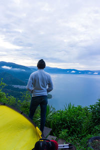 Rear view of man standing on mountain against sky