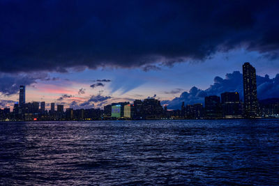 Sea by buildings against sky at sunset