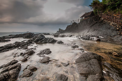 Rock formations at beach against cloudy sky