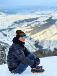 Side view of man sitting on snow covered mountain