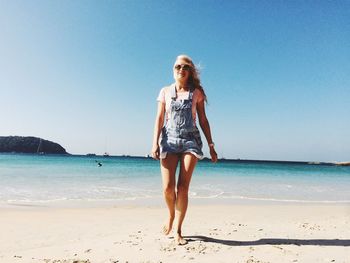 Full length of young woman walking at beach against clear sky