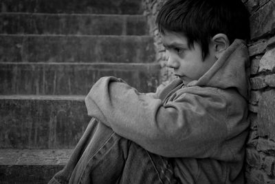 Side view of sad boy looking away while sitting outdoors