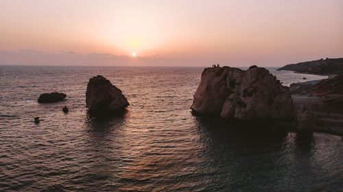 Rocks in sea against sky during sunset