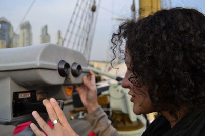 Side view of woman looking through binoculars in city