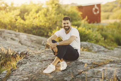 Portrait of smiling man sitting on rock formation during sunny day