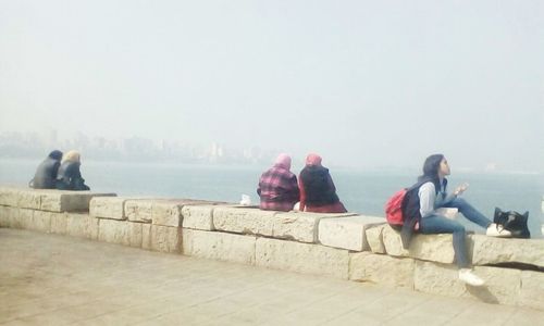 People sitting on promenade looking at sea against sky