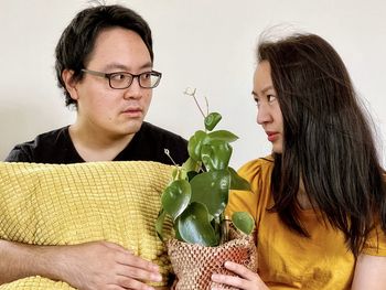 Young asian man and woman exchanging looks while holding potted pilea plant.