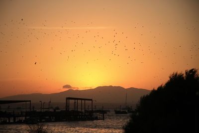 Silhouette pier on sea against orange sky during sunset