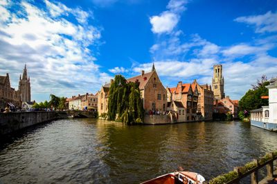 Boat moored at river by houses against sky