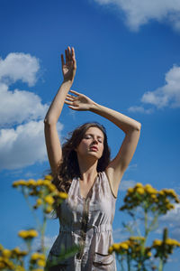 Young woman with arms raised standing against sky