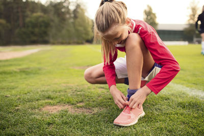 Girl crouching while tying shoelace on soccer field