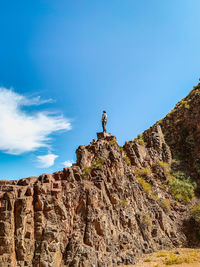 Low angle view of person standing on rock against sky