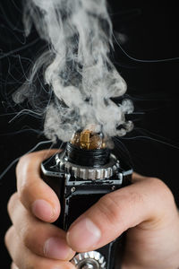 Close-up of hand holding electronic cigarette against black background