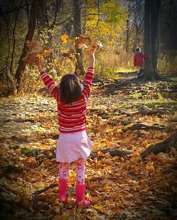 Full length rear view of girl holding leaves while standing on tree trunk