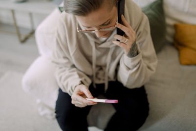 High angle view of lesbian woman talking on smart phone while holding pregnancy test results at home