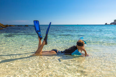 Side view of woman wearing diving flippers while lying in sea on shore