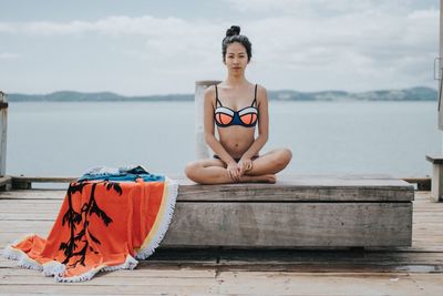 Young woman sitting by sea against sky