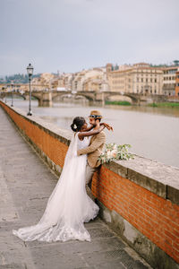 Woman holding umbrella while standing on bridge over canal