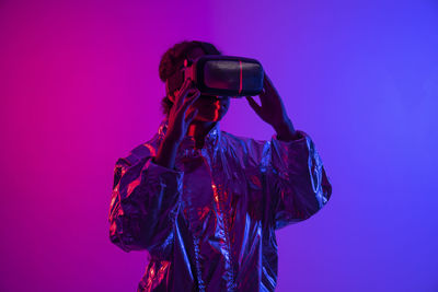 Young woman wearing virtual reality simulator standing against multi-colored background