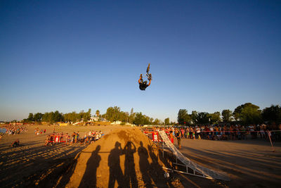 People flying over road against clear blue sky