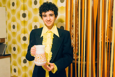 Portrait of smiling boy holding jug standing at home