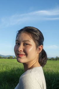 Portrait of smiling young woman on field against sky