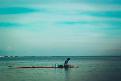 Boy sitting on raft over sea against sky