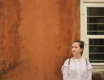 Portrait of young woman standing against wall