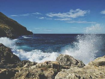 Waves splashing on rocky shore against sky