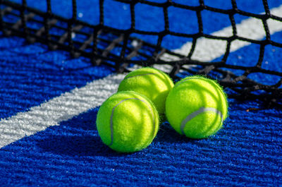 Three balls near the net of a blue padel tennis court, racket sports concept
