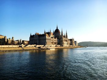 Danube river by hungarian parliament building in city against clear sky