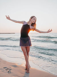 Full length of young woman dancing at beach during sunset