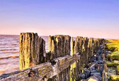 Abandoned wooden fence by sea during sunset