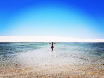 Rear view of woman with arms outstretched standing in sea against clear sky