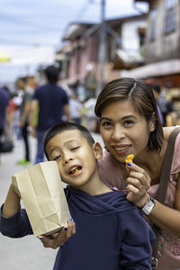 Portrait of smiling mother with son eating popcorn while standing on street in city