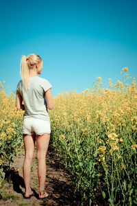 Rear view full length of young woman standing at oilseed rape