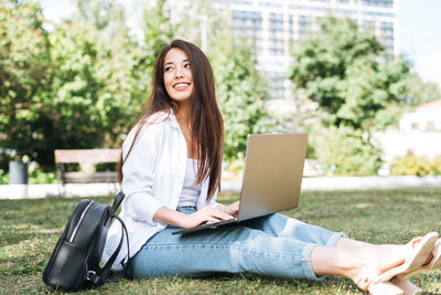 Young asian woman student freelancer with long hair working on laptop in city park