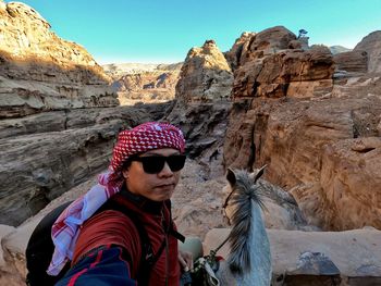 Midsection of man wearing hat on rock against sky