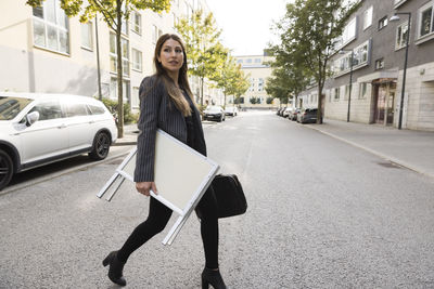 Female real estate agent carrying placard while crossing street in city