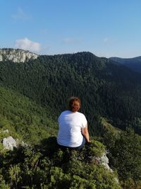 Rear view of woman sitting on mountain against sky