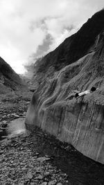 Woman resting on rock formation at fox glacier against cloudy sky