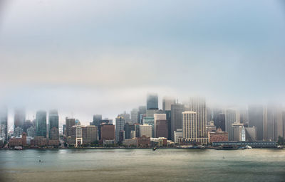 Sea by modern buildings in city against sky