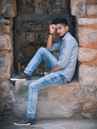 Portrait of young man sitting against stone wall