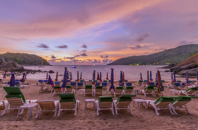 Chairs and umbrella arranged at beach against cloudy sky during sunset