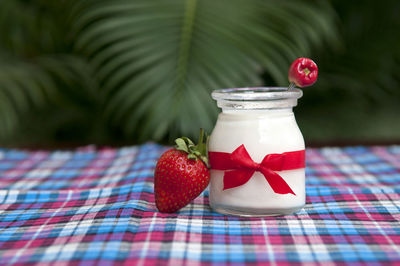 Jar with yogurt and strawberries on tablecloth