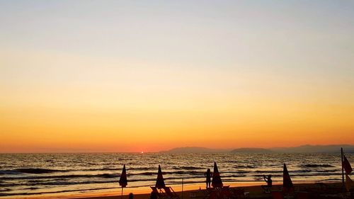 Silhouette people on beach against sky during sunset