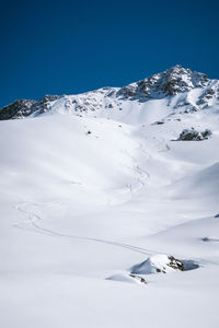 Fresh ski tracks in powder in front of snowcapped mountains against clear sky