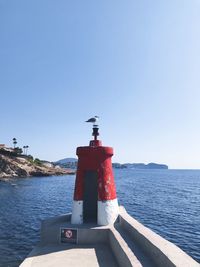 Lighthouse by sea against clear sky